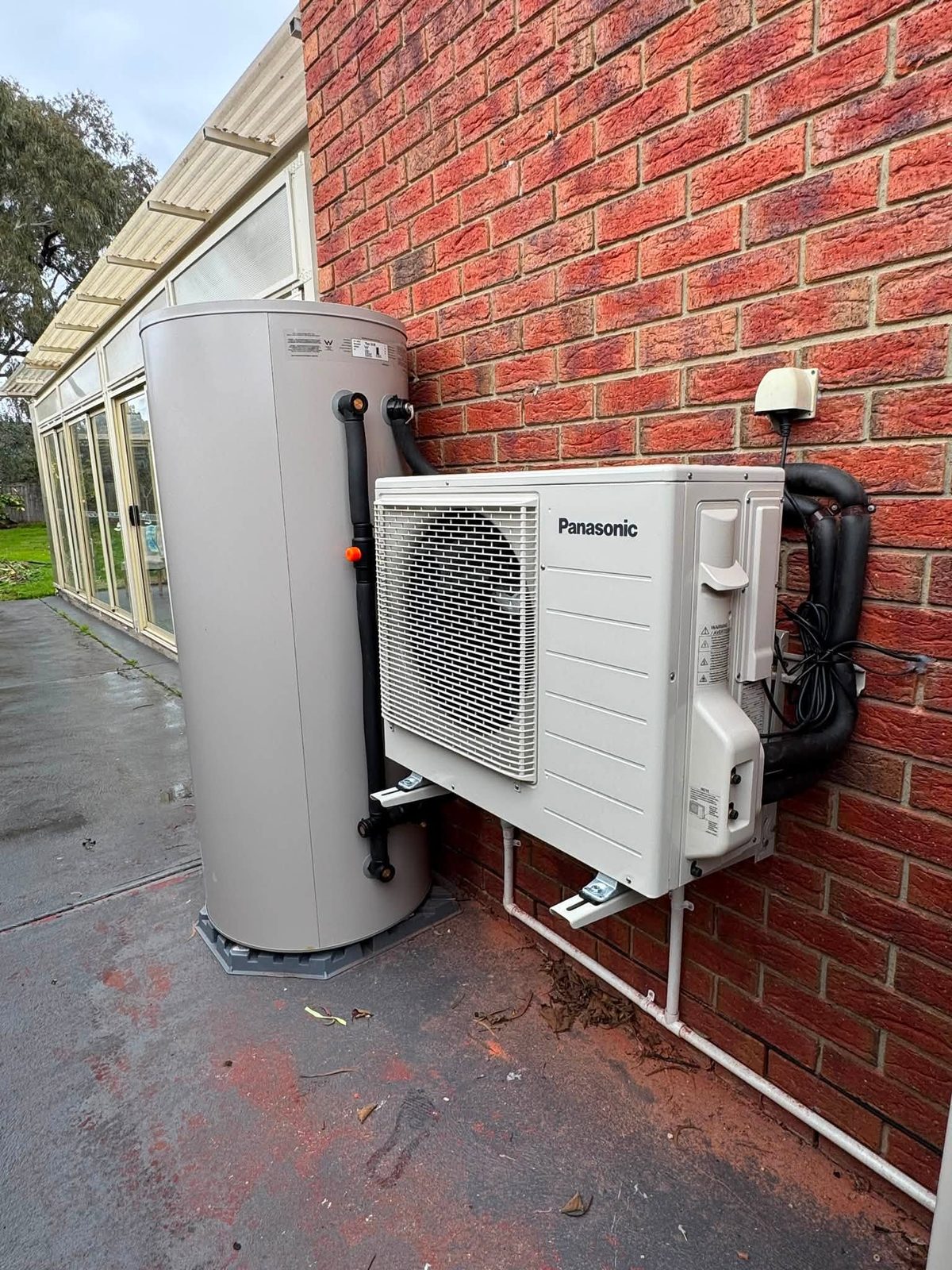 Panasonic CO₂ heat pump hot water system installed beside a brick home